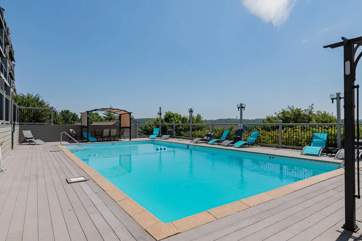 A vibrant exterior pool area with lounge chairs, a canopy, and surrounding greenery, presenting an inviting atmosphere for swimming, sunbathing, or socializing with friends. The open space is ideal for group gatherings or winding down after a day of Branson activities.