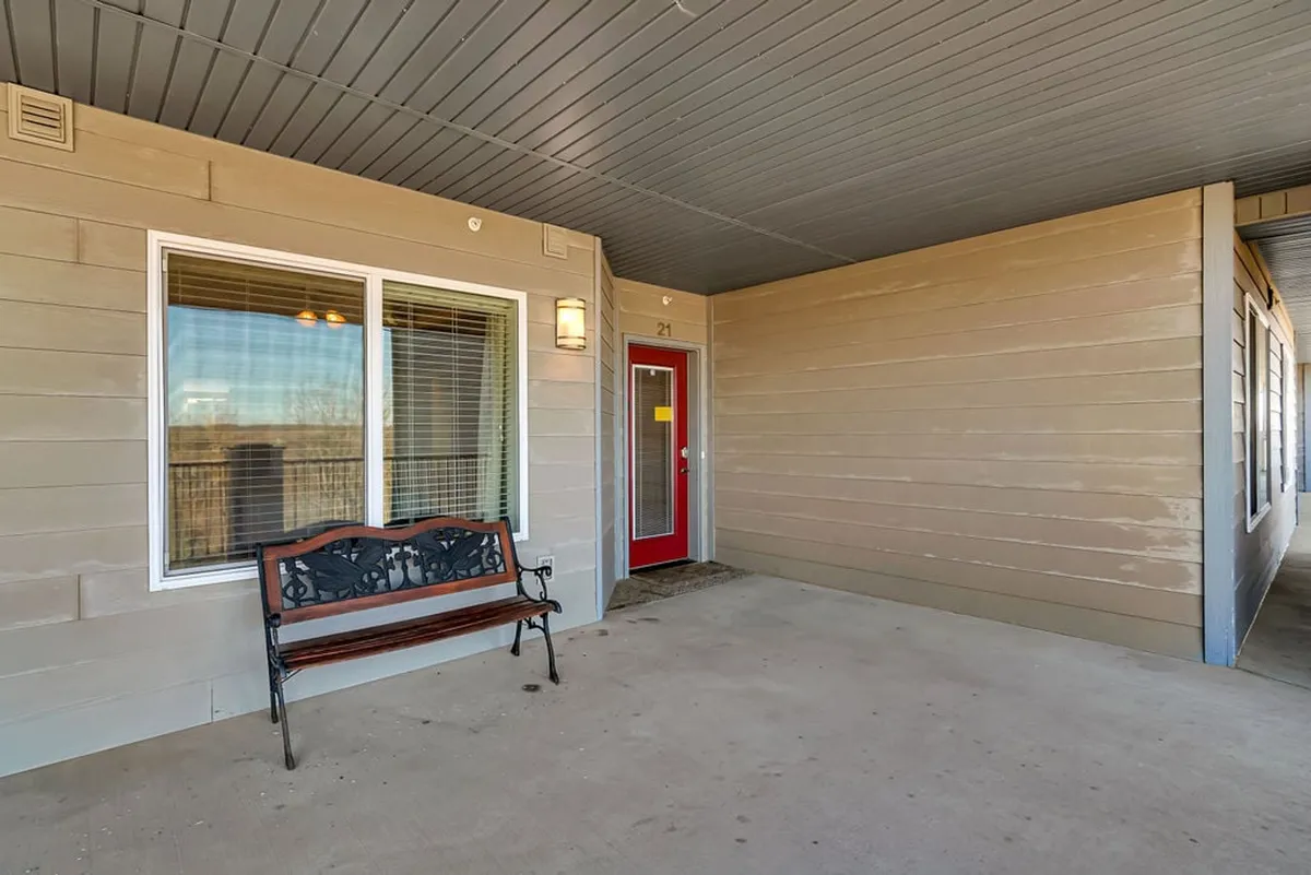 This image captures the inviting exterior of the property, with a red front door, decorative bench, and large windows. The bench provides a peaceful spot for couples to sit and enjoy the serene surroundings, while the door and windows hint at the cozy interior beyond.