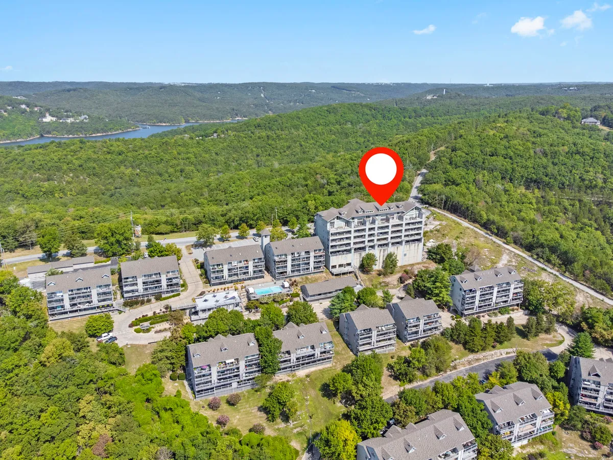 The image shows a multi-story building surrounded by lush greenery, with a swimming pool in the foreground. The peaceful atmosphere hints at possibilities for outdoor relaxation, nature walks, and group activities by the water or in nearby wooded areas. The building's balconies suggest private spaces for enjoying the views, tying into the section's mention of lakeside decks and tranquil views.