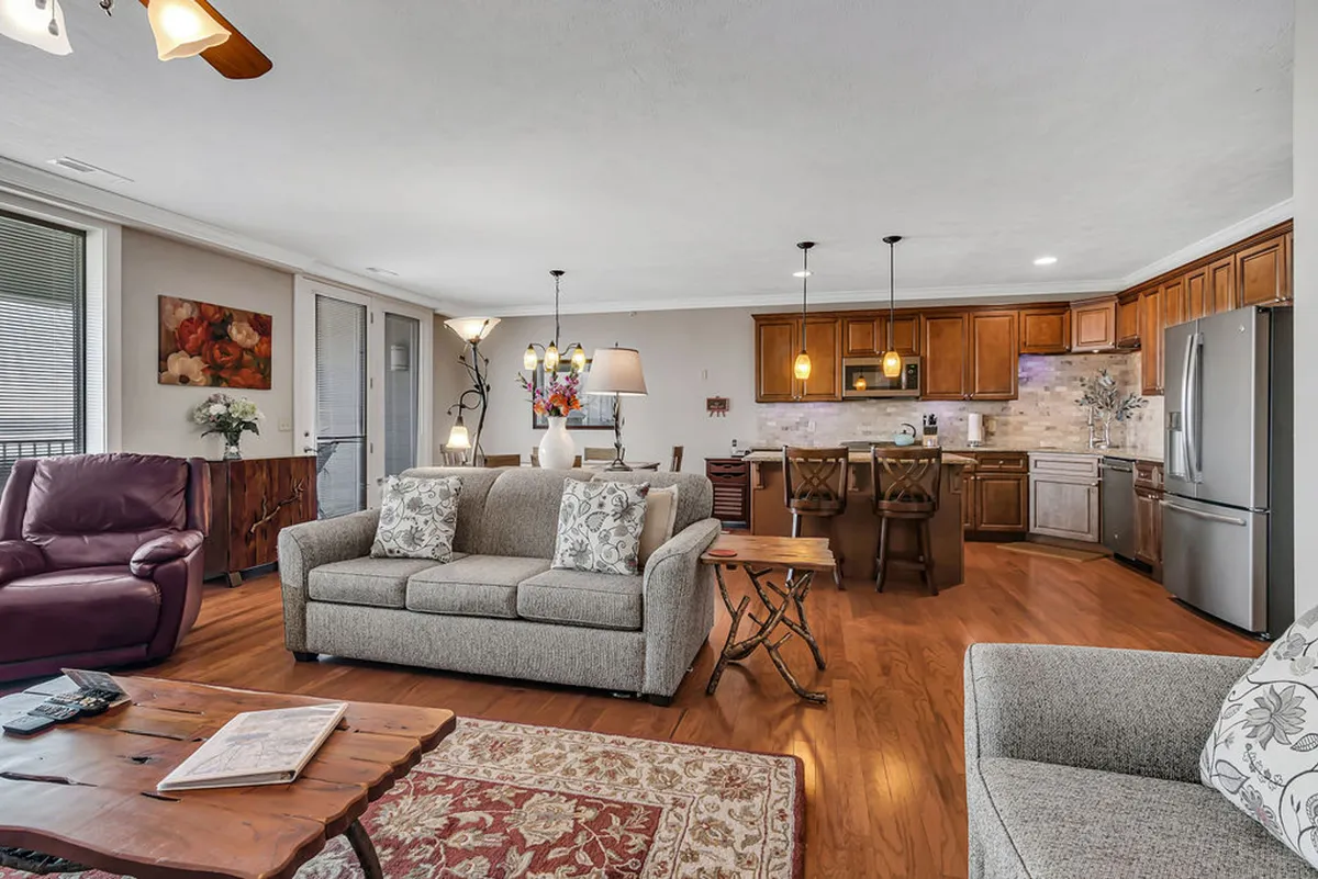 A spacious, open-plan interior connects a cozy living room and a kitchen with wood cabinetry. The soft lighting, patterned cushions, and thoughtful decor exude comfort, style, and functionality—all on a single, accessible level.