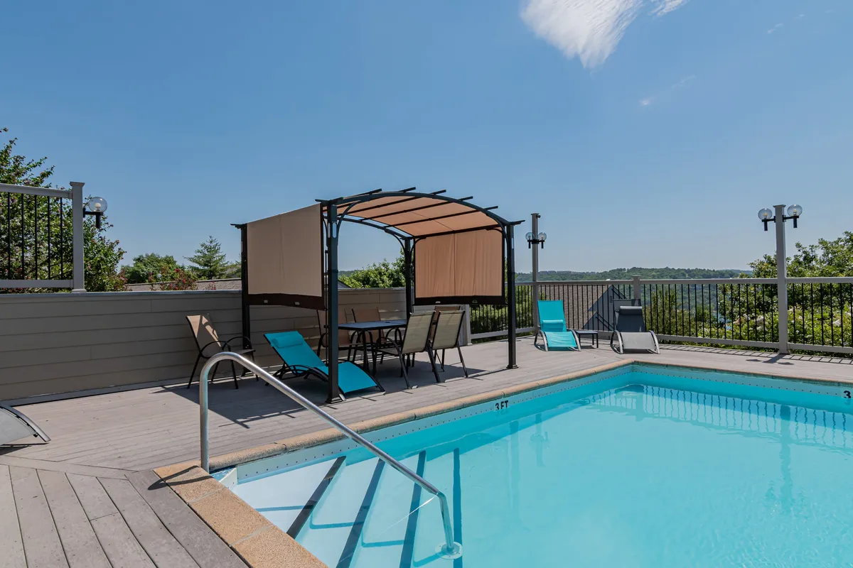 This exterior scene shows the inviting swimming pool area surrounded by a canopy seating area and natural landscape. The pool is a gathering spot for swimming, sunbathing, and socializing—activities that cater to guests of all ages.