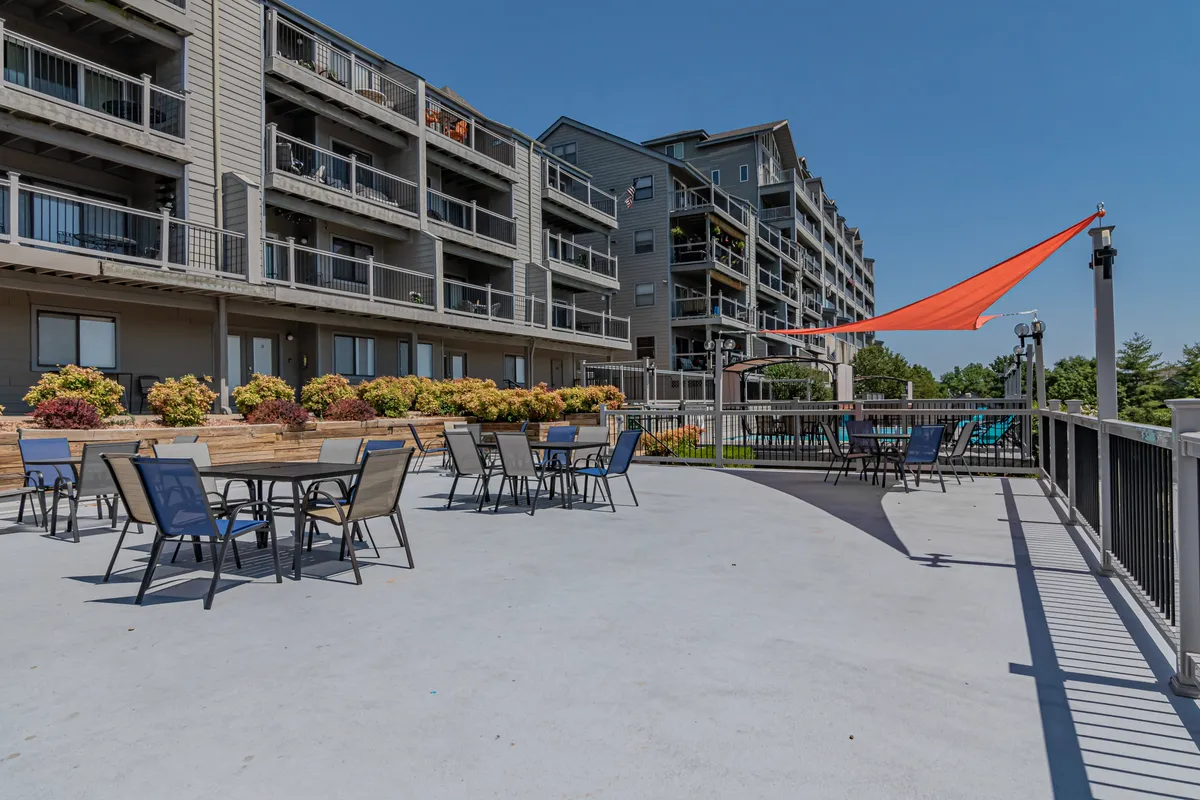 The cheerful outdoor seating area is adorned with a colorful sunshade and surrounded by vibrant flower beds. The setup encourages relaxation, al fresco dining, and spending quality time outdoors, possibly with sunset views over the lake.