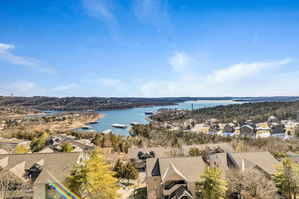 A tranquil view of Table Rock Lake framed by rolling hills, clustered homes, and abundant trees. The scene suggests opportunities for boating, fishing, hiking, and picnicking along the lakeshore, capturing the natural beauty and outdoor possibilities.