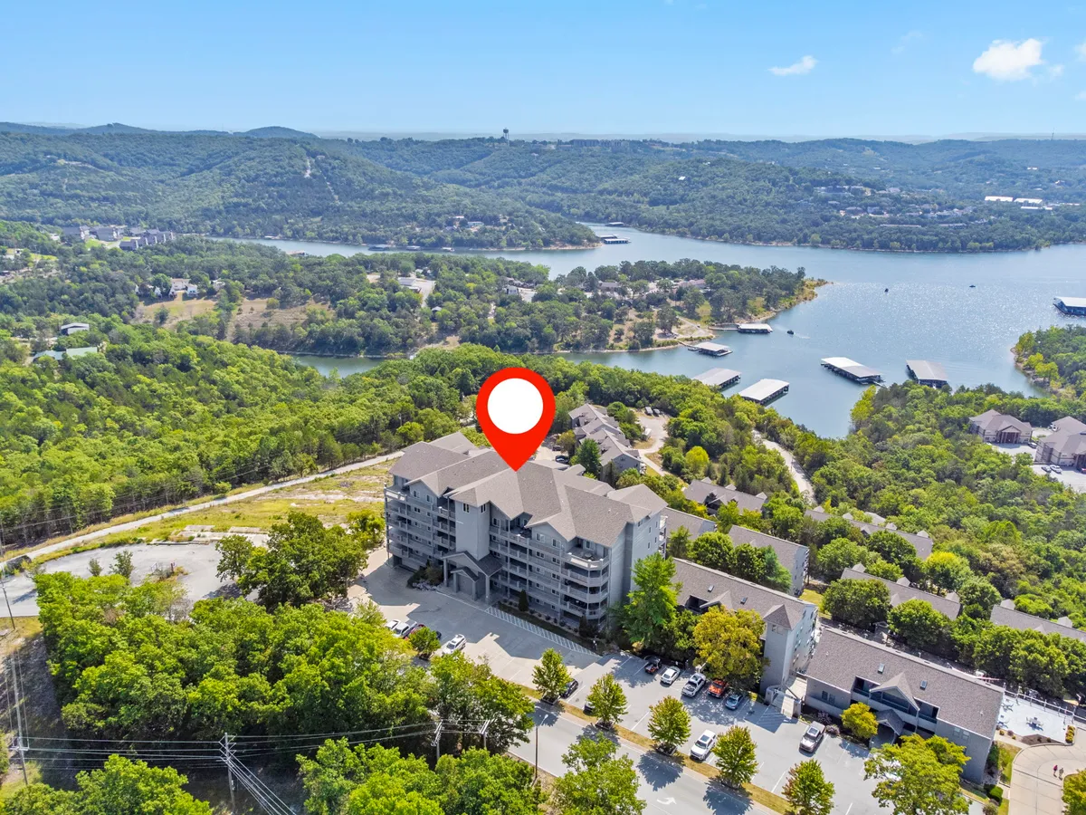 A wide exterior view showing the main building, lush greenery, water bodies, and rolling hills in the background. The natural surroundings highlight opportunities for boating, hiking, and exploring local nature trails near the property.