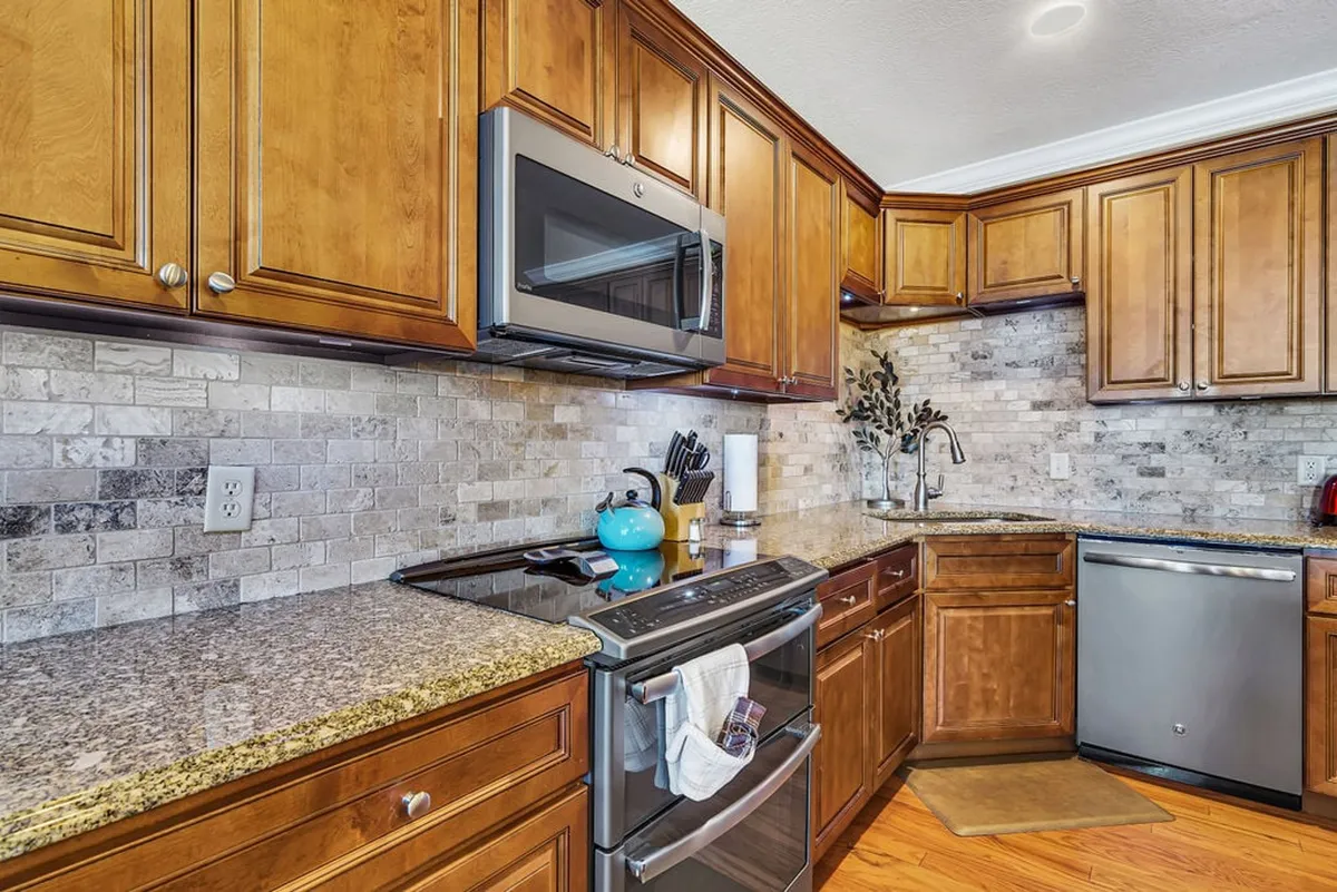 A modern kitchen is showcased with granite countertops, wooden cabinetry, stainless steel appliances, and a decorative plant. The scene highlights a practical, fully equipped kitchen that invites cooking, gathering, and enjoying meals together.