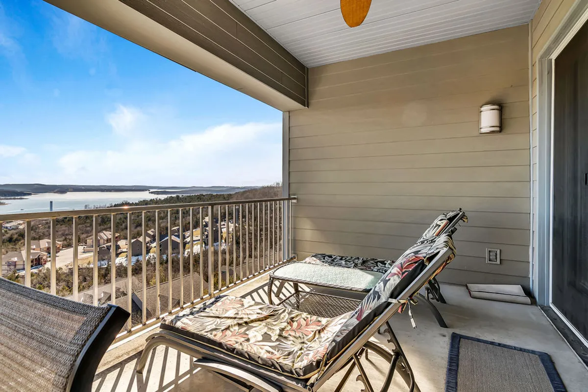 The image focuses on a private balcony with comfortable chairs overlooking a serene lake, complemented by a ceiling fan. The mood is peaceful, suggesting opportunities for guests to relax, sip morning coffee, or enjoy evening breezes while taking in the lake views.