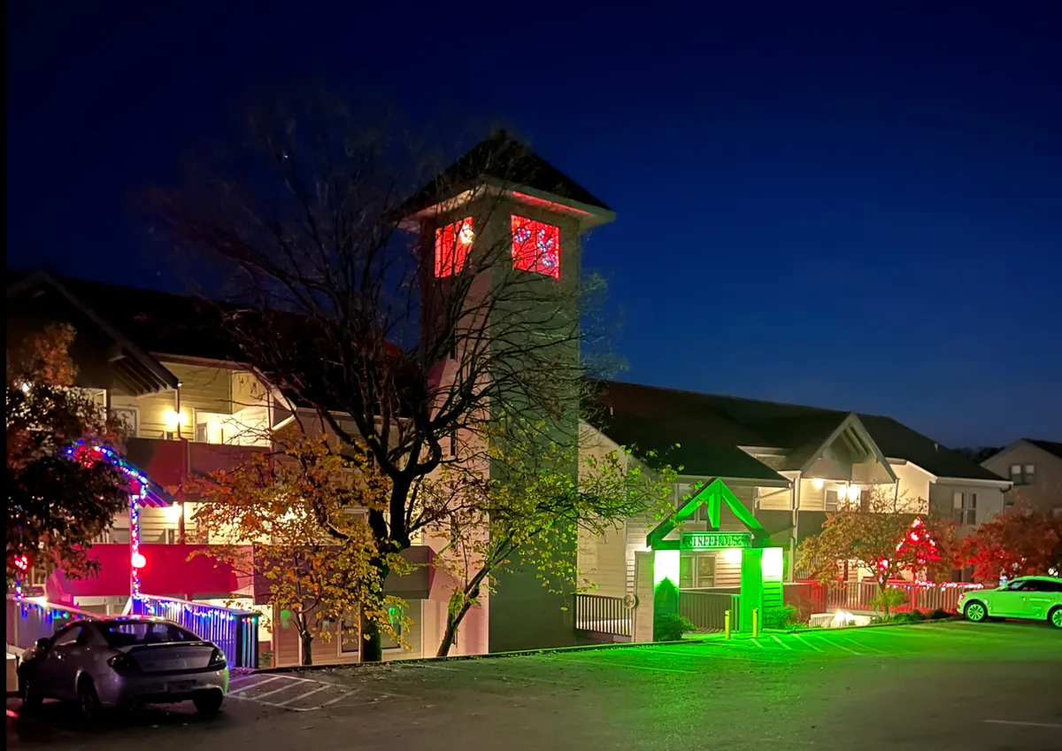 A tall clock tower with red windows and a green illuminated entrance creates a magical, inviting scene. Decorative lights add a festive touch, making the area perfect for evening walks or celebrating special moments together.