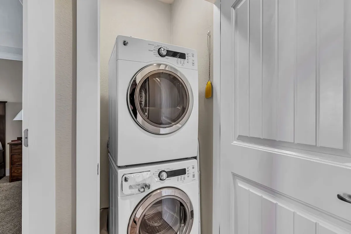 A bright, organized laundry closet features a stacked washer and dryer framed by clean white cabinetry, conveying a sense of convenience and tidiness. The setting suggests an easy routine for keeping clothes fresh at any point during a stay.