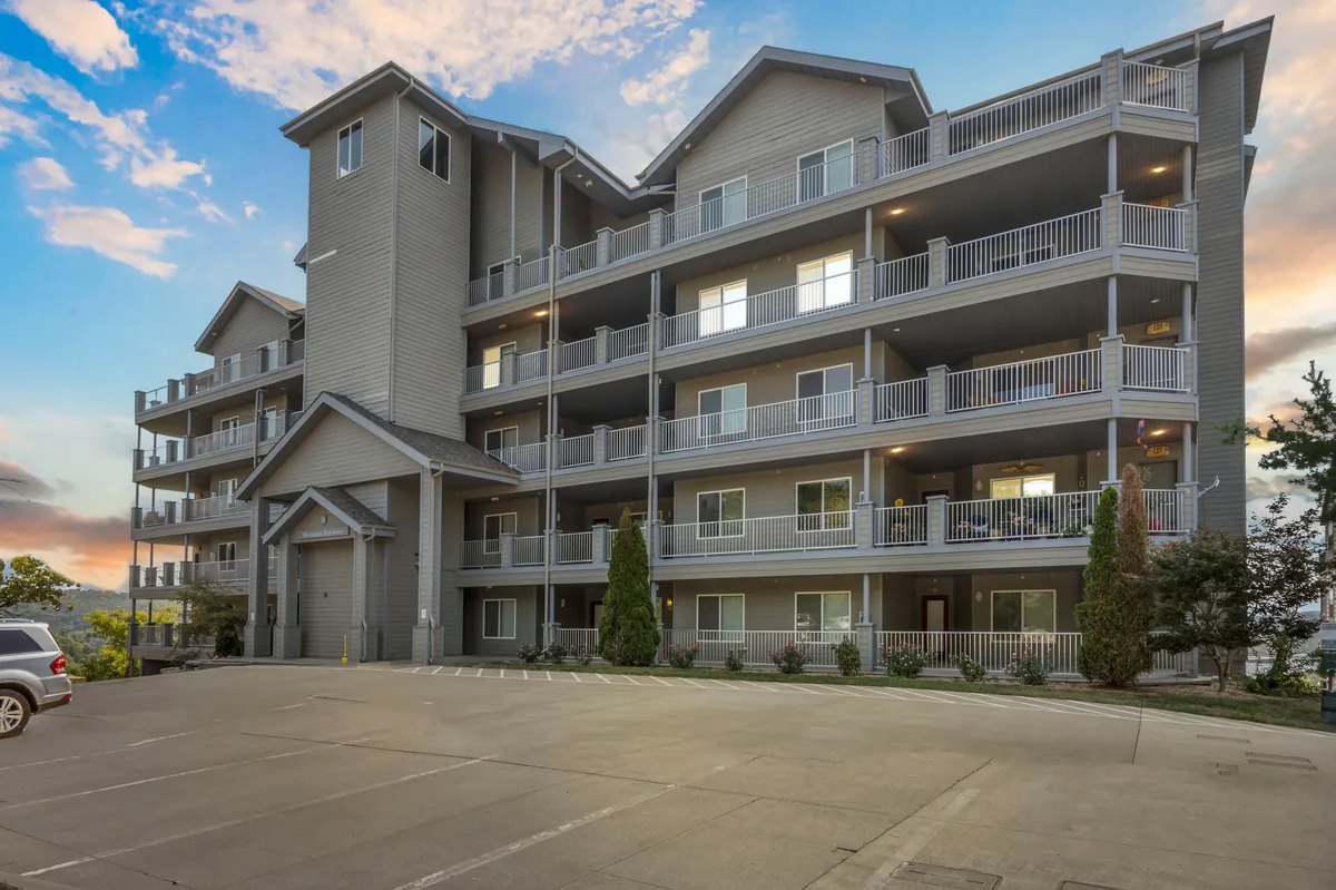 The image depicts a welcoming building exterior with balconies and lush landscaping. Several balconies offer spots for relaxing outdoors, while the landscaped entrance gives a sense of friendly community and convenient access to local attractions.